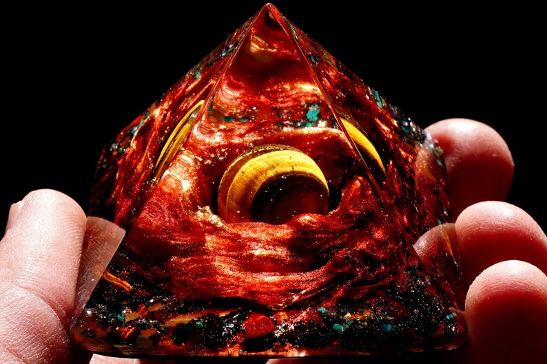 May include: A red, gold, and blue pyramid-shaped crystal with a swirling pattern inside. The crystal is made of resin and has a shiny, glossy finish.