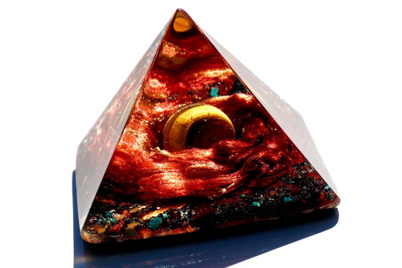 May include: A red, gold, and blue resin pyramid with a gold orb inside. The pyramid is on a blue base.