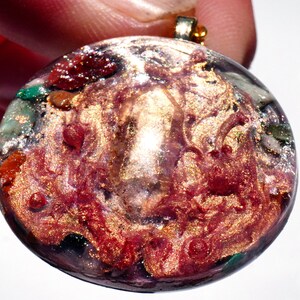 May include: Round pendant necklace with a gold chain. The pendant is made of clear resin with a swirling mix of red, gold, and green glitter.