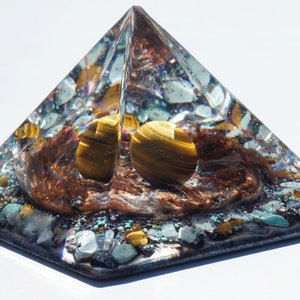 May include: A clear pyramid with a brown, gold, and blue crystal inside. The pyramid is made of resin and has a smooth, polished finish.