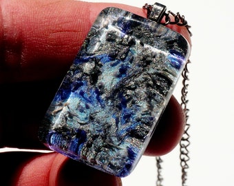May include: A silver chain necklace with a rectangular pendant made of clear glass with blue and silver swirls inside.