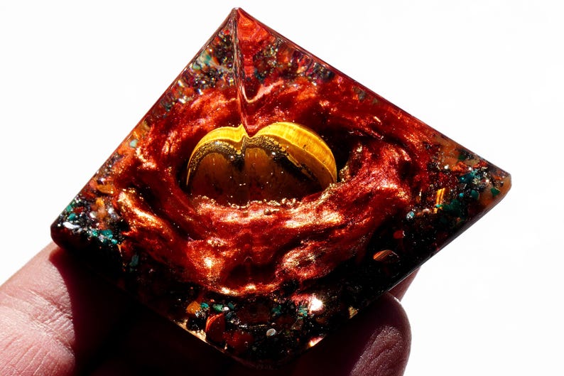 May include: A red, orange, and green crystal pyramid with a yellow and gold crystal inside. The pyramid is made of clear resin and has a shiny, metallic finish.