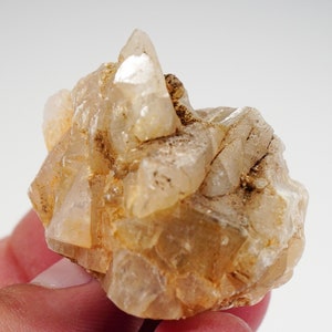 May include: A cluster of clear, translucent quartz crystals with a light brown, earthy hue. The crystals are clustered together in a rough, natural formation.