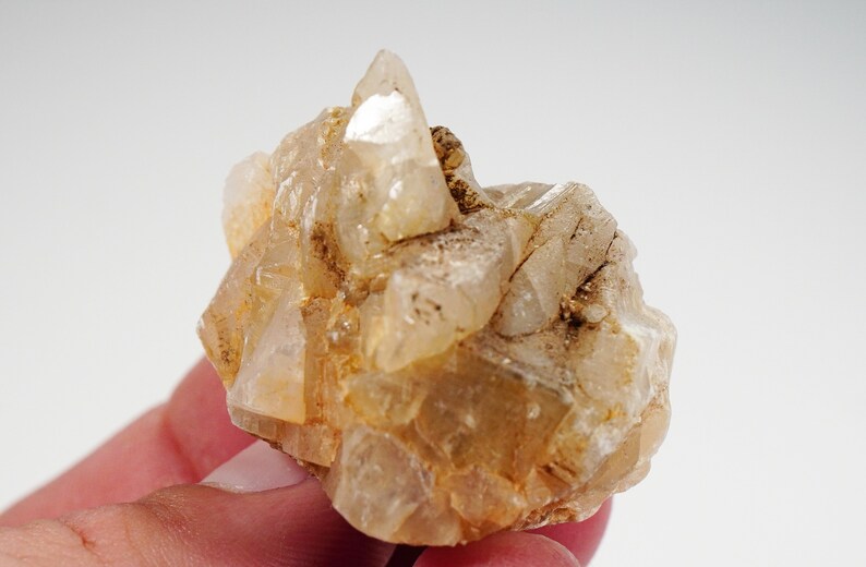 May include: A cluster of clear, translucent quartz crystals with a light brown, earthy hue. The crystals are clustered together in a rough, natural formation.