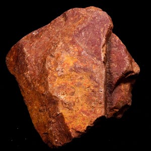 Könnte beinhalten: Eine raue, rotbraune Felsformation mit strukturierter Oberfläche. Der Felsen hat eine natürliche, organische Form und ist vor einem schwarzen Hintergrund platziert. Die Farbe variiert von tiefem Rot bis zu helleren Orangetönen.