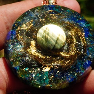May include: A round, blue, green, and gold pendant with a white, iridescent stone in the center. The pendant is made of resin and has a gold chain.