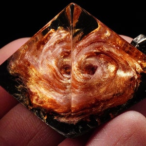 May include: A gold and pink resin pyramid pendant with a swirling galaxy design. The pendant is clear and has a black border.