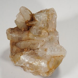 May include: A cluster of translucent, light brown crystals with a rough, natural texture. The crystals are clustered together in a random, organic shape.