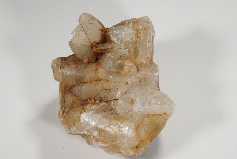 May include: A cluster of translucent, light brown crystals with a rough, natural texture. The crystals are clustered together in a random, organic shape.