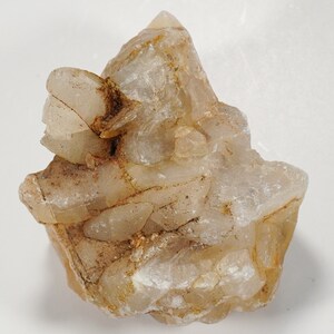 May include: A cluster of clear quartz crystals with a light brown tint. The crystals are clustered together in a rough, natural formation.