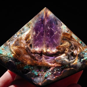 Può includere: Un cristallo di ametista viola è racchiuso in una piramide di resina trasparente con accenti dorati e turchesi. La piramide è un oggetto decorativo per l'arredamento della casa o la guarigione con i cristalli.
