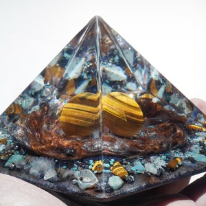 May include: A clear pyramid-shaped crystal with a brown, gold, and blue interior. The crystal contains small pieces of various stones, including tiger's eye, turquoise, and copper.