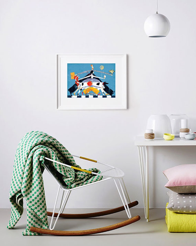 May include: A framed illustration of a colorful abstract scene with a white rocking chair and a green and white blanket draped over it. The illustration features a blue background with a white, orange, and yellow figure in the center. There is a white table with a white lamp and a stack of colorful pillows.