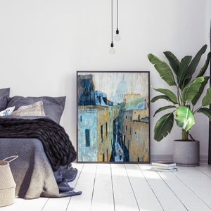 May include: A painting of a Parisian street scene with a view of the Sacr&eacute;-C&oelig;ur Basilica in the distance. The painting is in a black frame and is hanging on a white wall.