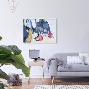May include: A gray sofa with a white throw blanket and two pillows, one with a white and gray pattern and the other with a white and blue pattern. A small wooden table with a record player and a framed abstract art print with a blue and white color scheme hangs on the wall behind the sofa.