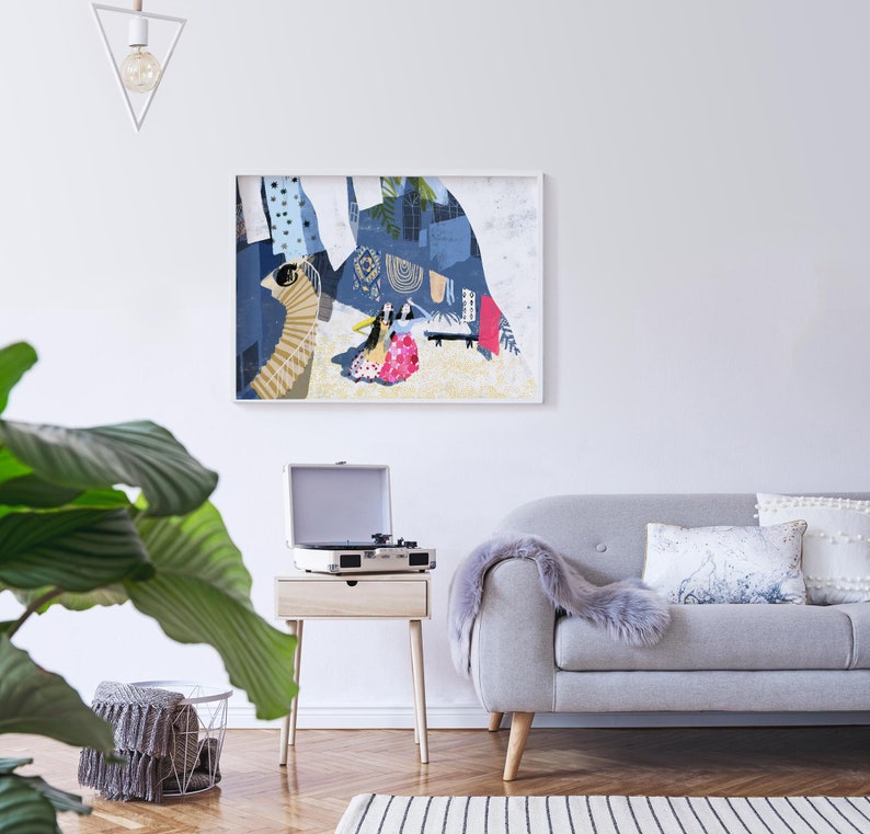May include: A gray sofa with a white throw blanket and two pillows, one with a white and gray pattern and the other with a white and blue pattern. A small wooden table with a record player and a framed abstract art print with a blue and white color scheme hangs on the wall behind the sofa.