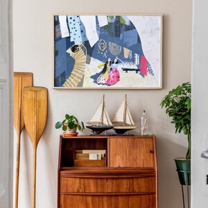 May include: A wooden vintage style secretary desk with three drawers and a top shelf. The desk is decorated with two small sailboats, a potted plant, and a glass bottle. A framed abstract painting with a blue, white, and pink color scheme hangs on the wall behind the desk.