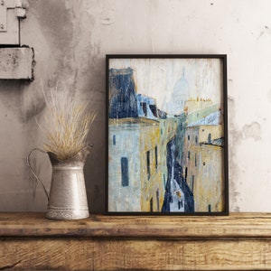 May include: A framed painting of a Parisian street scene with buildings and a church in the background. The painting is done in a watercolor style with a light blue and gray color scheme.