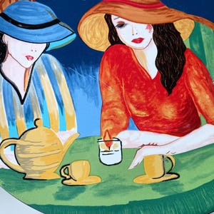 Furio Café plates displayed together: a large oval dinner plate featuring two women seated at a café table with a yellow teapot and cups, with bold, colorful artwork