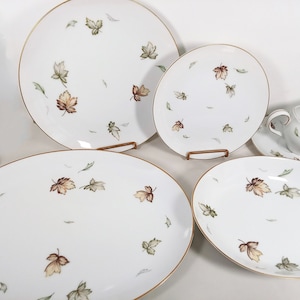 May include: A set of five white porcelain plates with a gold rim and a delicate pattern of brown and green leaves. The set includes a large oval platter, a smaller oval platter, a dinner plate, a salad plate, and a gravy boat with a matching saucer.
