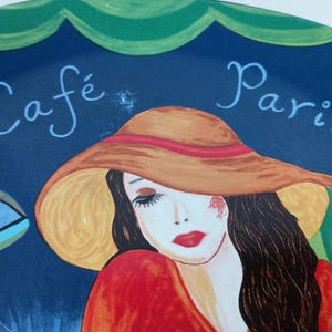 Furio Café plates displayed together: a large oval dinner plate featuring two women seated at a café table with a yellow teapot and cups, with bold, colorful artwork with
