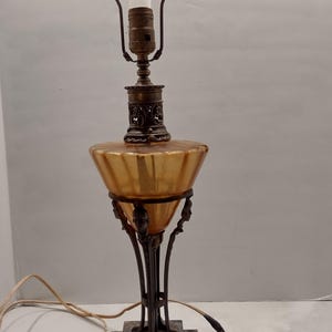 Antique Egyptian Revival lamp before cleaning, showing amber‑toned glass font darkened by oil and smoke residue, ornate metal column, and stepped marble base with original wiring visible.
