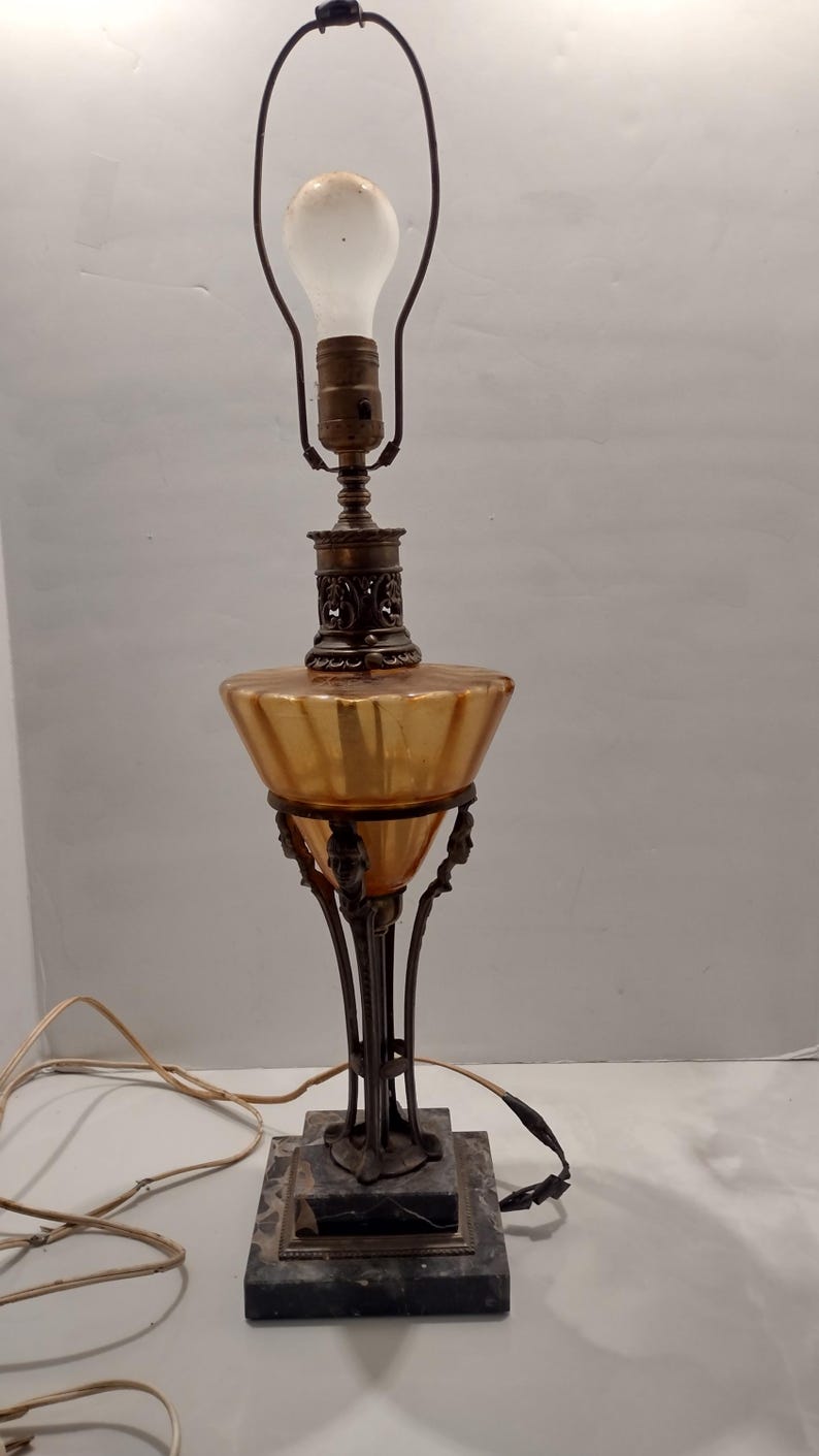 Antique Egyptian Revival lamp before cleaning, showing amber‑toned glass font darkened by oil and smoke residue, ornate metal column, and stepped marble base with original wiring visible.