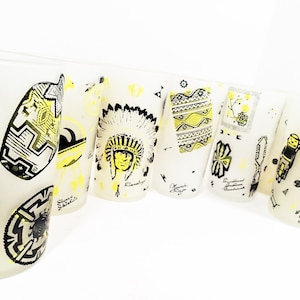 May include: A set of eight white glass tumblers with black and yellow Native American inspired designs. The designs include a headdress, a geometric pattern, and a stylized figure.