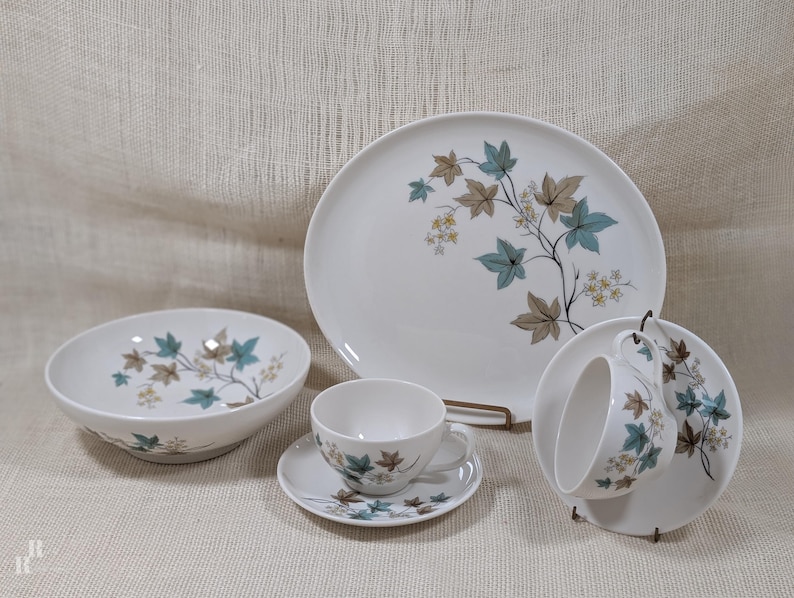 Mid‑century Syracuse China Woodbine pieces including an oval platter, serving bowl, and two cup‑and‑saucer sets with the aqua and brown floral motif on a bright white glaze.