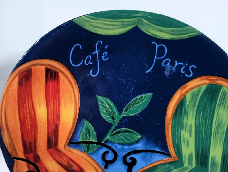 Furio Café salad plates display colorful empty chairs sitting at a French Cafe scene with two colorful and a cafe table