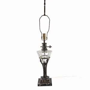 Complete Egyptian Revival table lamp rebuilt from parts of two originals, showing stepped black marble base, ornate metal column, clear glass font, and brass socket with harp.