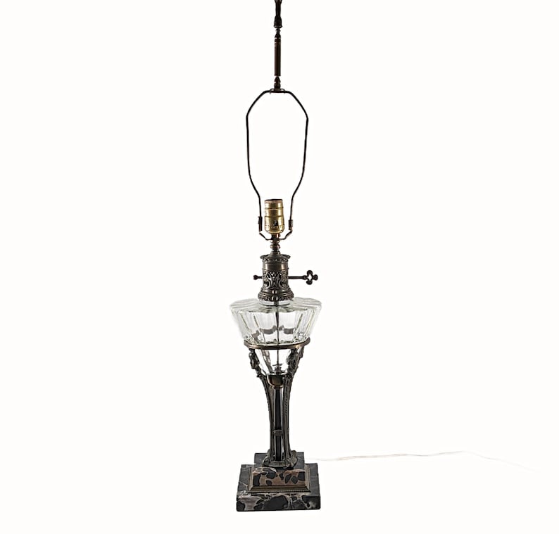 Complete Egyptian Revival table lamp rebuilt from parts of two originals, showing stepped black marble base, ornate metal column, clear glass font, and brass socket with harp.