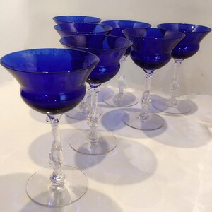 MSet of 7 Antique Cobalt Royal Blue 3126 Cambridge Glass Champagne / Tall Sherbet Stemware.  Beautiful, clear cobalt blue art deco style angular flare top on a bulbous, bulging bowl with graceful foliated clear glass tall stems.ay include: Set of six cobalt blue stemmed glasses with clear glass stems and bases. The glasses have a wide bowl and a delicate, twisted stem.