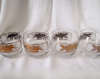 May include: Four clear, stemless glasses with a gold and black crown design. The glasses have a rounded shape and are set against a white background. The crown design is repeated on each glass.