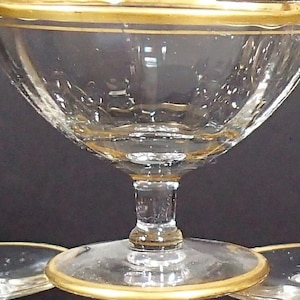 May include: Clear glass dessert dishes with gold rims. The stemware has a classic design with a wide bowl and a short stem. The gold rim adds a touch of elegance to the glassware. The dishes are likely used for serving desserts or small portions.