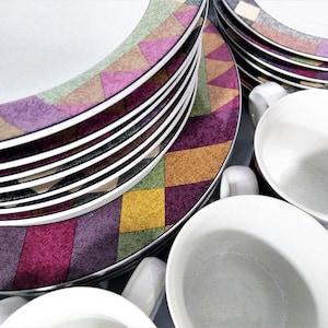 May include: A set of ceramic dinner plates and bowls with a geometric pattern in shades of purple, green, yellow, and brown. The plates are stacked on top of each other, and the bowls are placed in front of them.