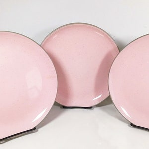 May include: Three pink dinner plates with a speckled glaze and a gray rim.