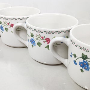 May include: Four white ceramic mugs with a floral design featuring blue and pink flowers, green leaves, and a green vine pattern.
