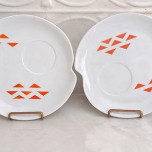 Pair or Jonas Roberts Japan snack plates with a white yin yang shape with orange diamonds on a white background and around indent to hold a cup or perhaps a little bowl of dipping sauce.

s
