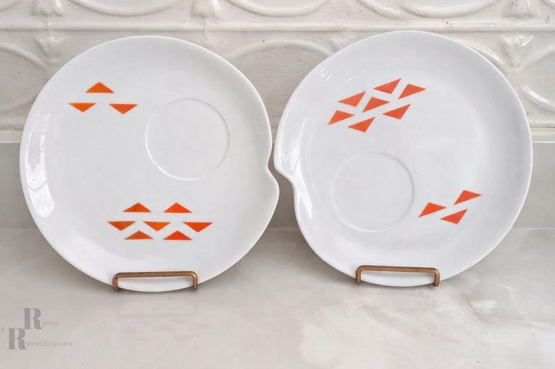 Pair or Jonas Roberts Japan snack plates with a white yin yang shape with orange diamonds on a white background and around indent to hold a cup or perhaps a little bowl of dipping sauce.

s