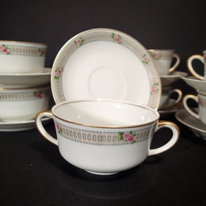 May include: Set of six white porcelain teacups and saucers with a gold trim and pink rose pattern. The cups have two handles and are perfect for serving tea or coffee.