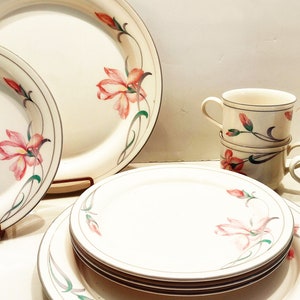 May include: A set of white ceramic dinnerware with a floral design featuring pink flowers and green leaves. The set includes a large dinner plate, a smaller dinner plate, and a set of four teacups.