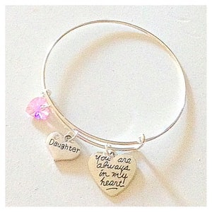 May include: Silver bangle bracelet with a pink crystal charm and two heart charms. One heart charm says "Daughter" and the other says "You are always in my heart".