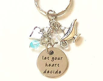 May include: A silver keychain with a charm that says "let your heart decide". The charm is surrounded by a small silver heart, a clear crystal, a blue crystal, and a gold genie lamp charm.