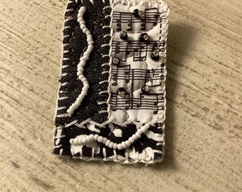 Black and white beaded musical pin brooch.