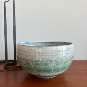 May include: A white ceramic bowl with a green and brown design. The bowl has a rounded shape and a wide rim.