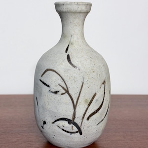 May include: A small, off-white ceramic vase with a speckled texture and a narrow neck. The body of the vase is decorated with hand-painted, thin black lines forming abstract, organic shapes that resemble leaves or stems.