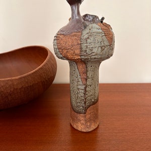 May include: A tall, ceramic vase with a unique, abstract design. The vase is brown, green, and white with a textured surface.