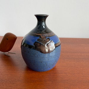 May include: A small, blue and black ceramic vase with a speckled glaze. The vase has a narrow neck and a rounded body.