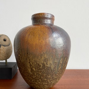 May include: A brown and black ceramic vase with a rounded shape and a textured surface.
